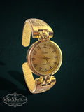 My Store Vivani gold-tone quartz cuff watch with a textured geometric band and round dial on a dark background.
