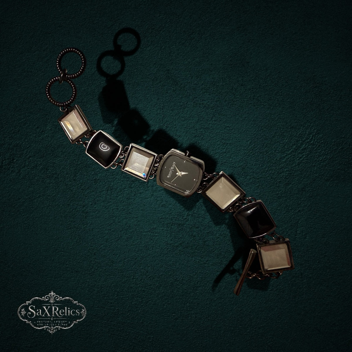 My Store White House Black Market link wristwatch with square glass and black resin accents on a dark green background.